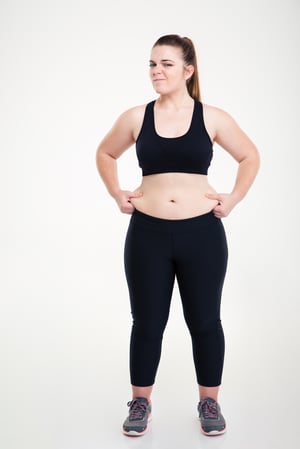 Full length portrait of a woman pinches fat on her belly isolated on a white background